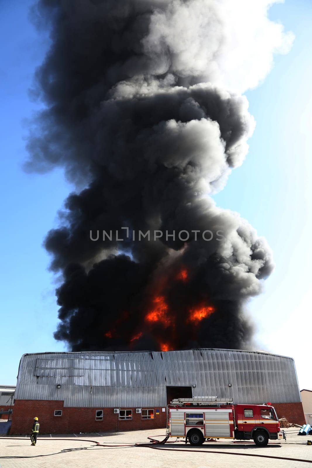 Warehouse building burning with intense flames and fireman attending