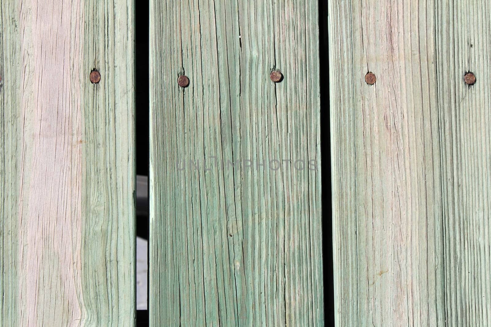 Closeup of nailed green tan wooden slats that make up an outdoor sidewalk on a sunny day..