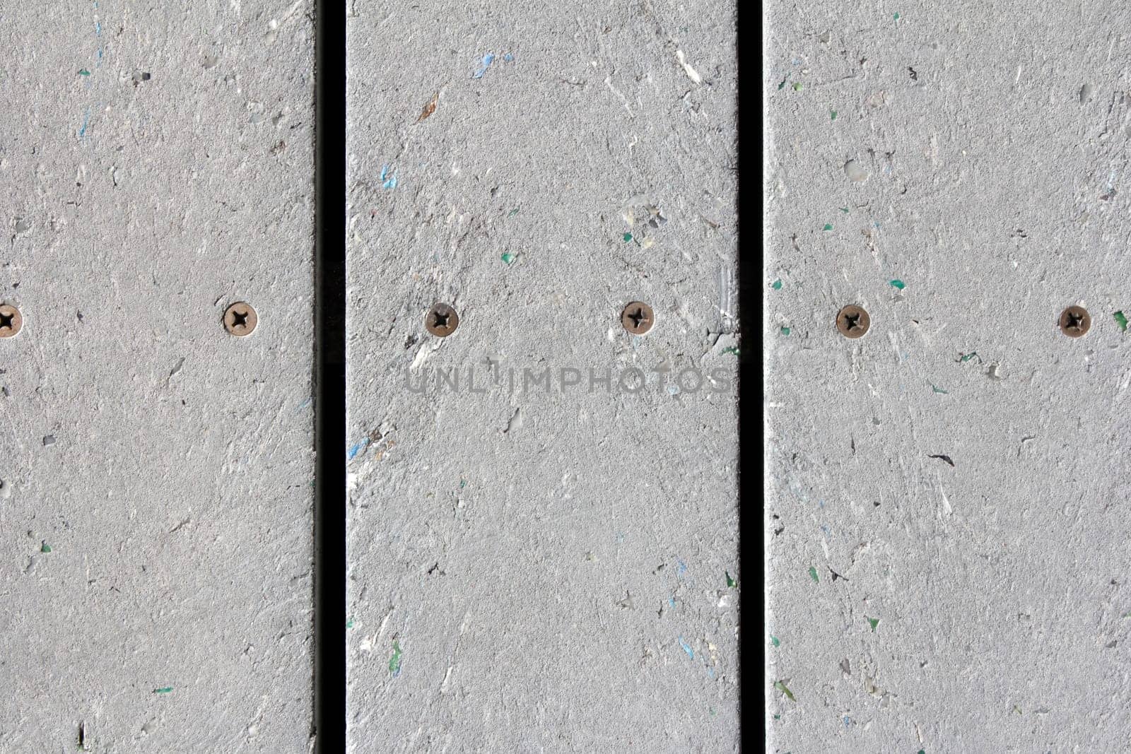 Close-up background of a sidewalk made of slats of recycled plastic composite that has been melted into being mostly uniformly gray but, with small speckles of color.