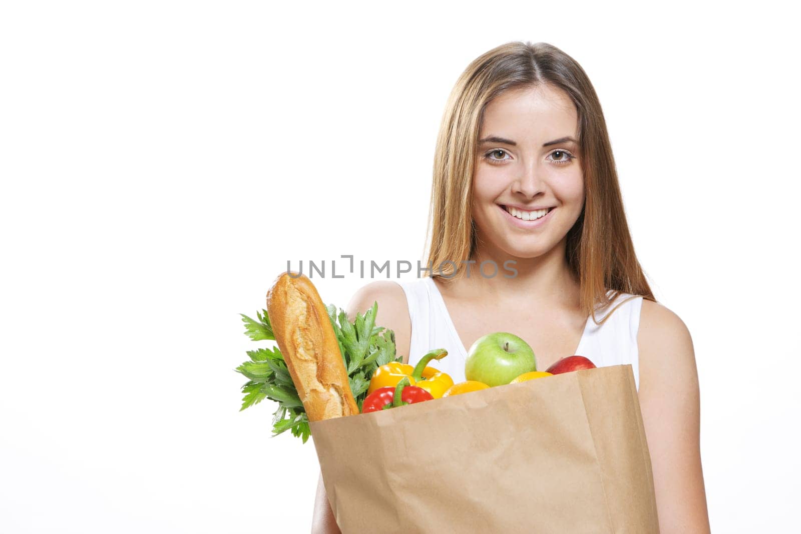 Portrait of smiling young woman holding a shopping bag full of groceries on white background