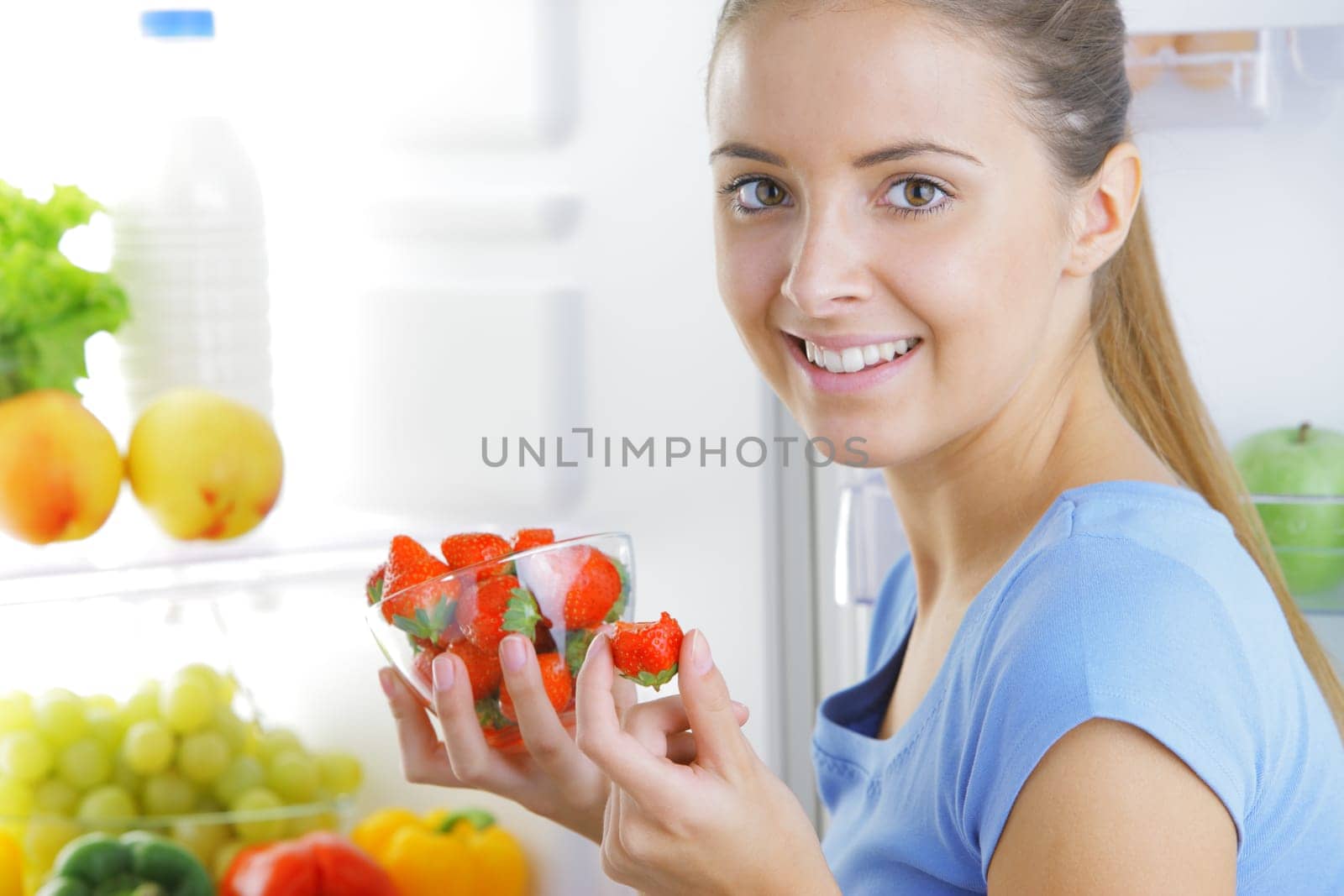 Smiling girl with strawberries near the refrigerator