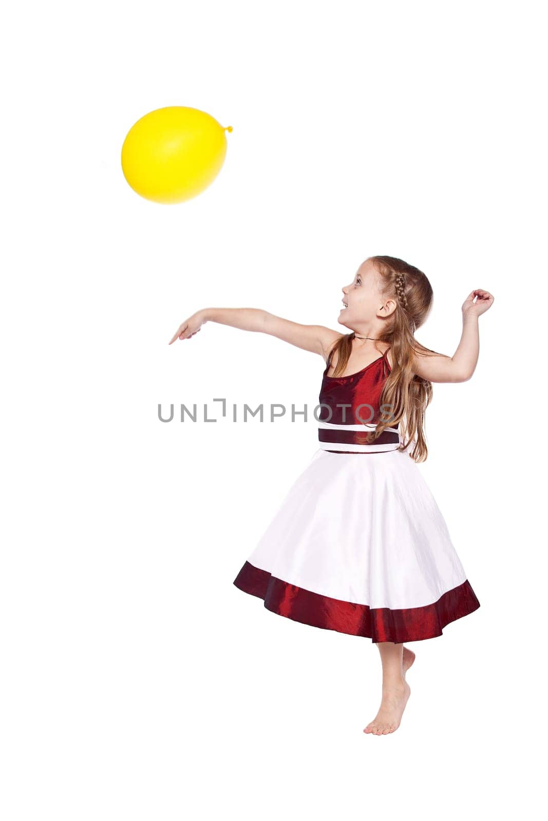 Laughing little girl in red and white dress playing with balloon