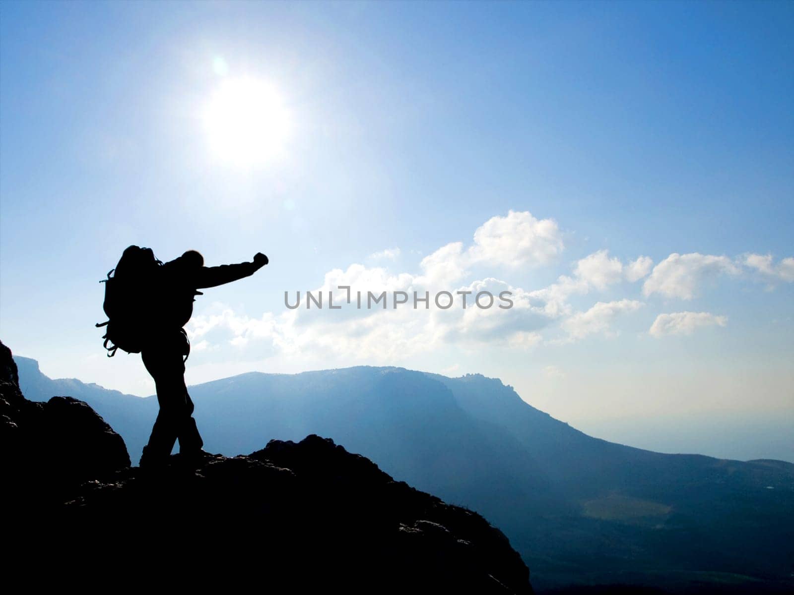 Hiker on top, silhouetted in high mountains