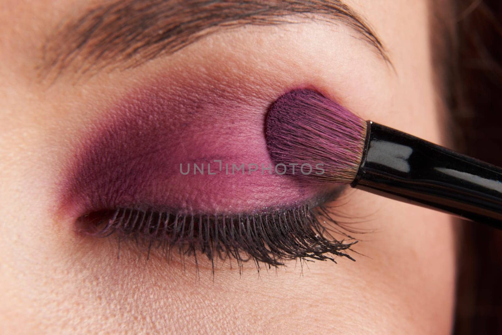 woman applying eye make-up with brush on white background