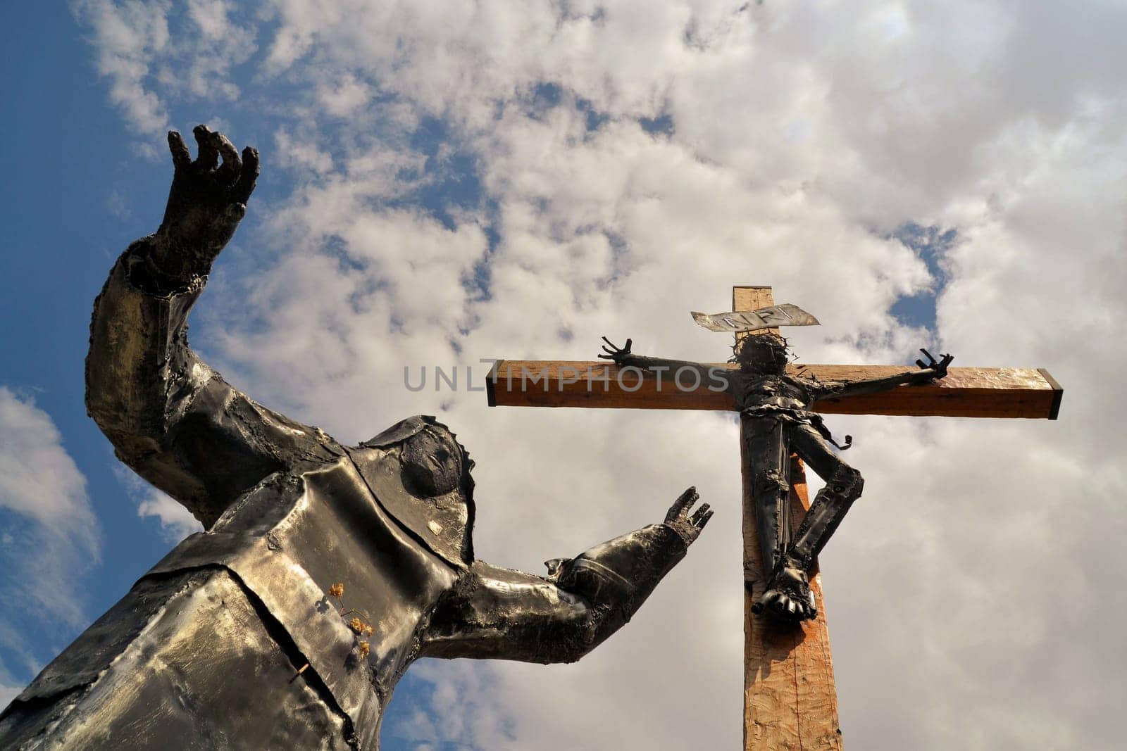 Modern steel statue of Christ with Virgin Mary lying at his feet against blue sky