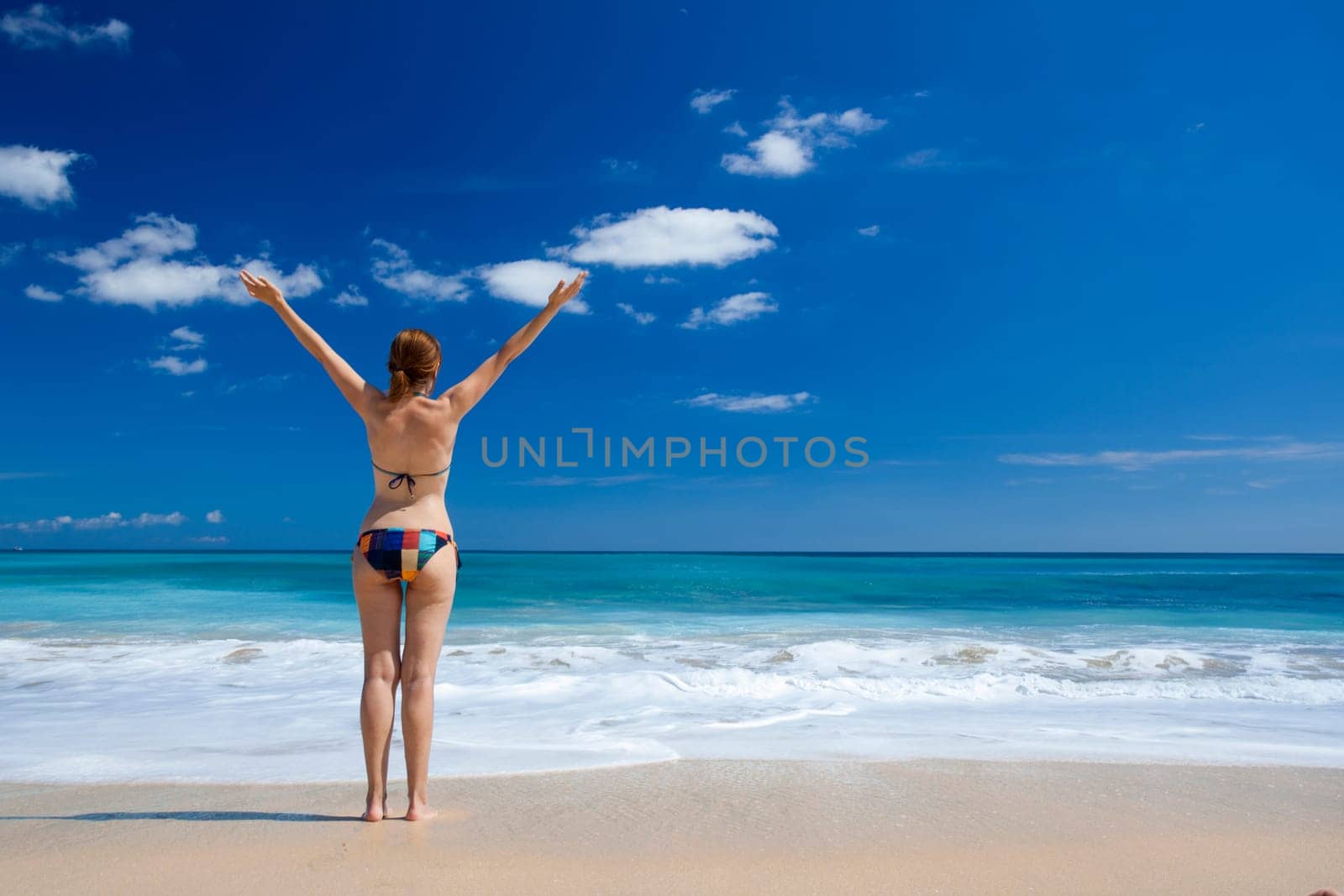 Beautiful young woman with arms open in a tropical beach enjoying the summer