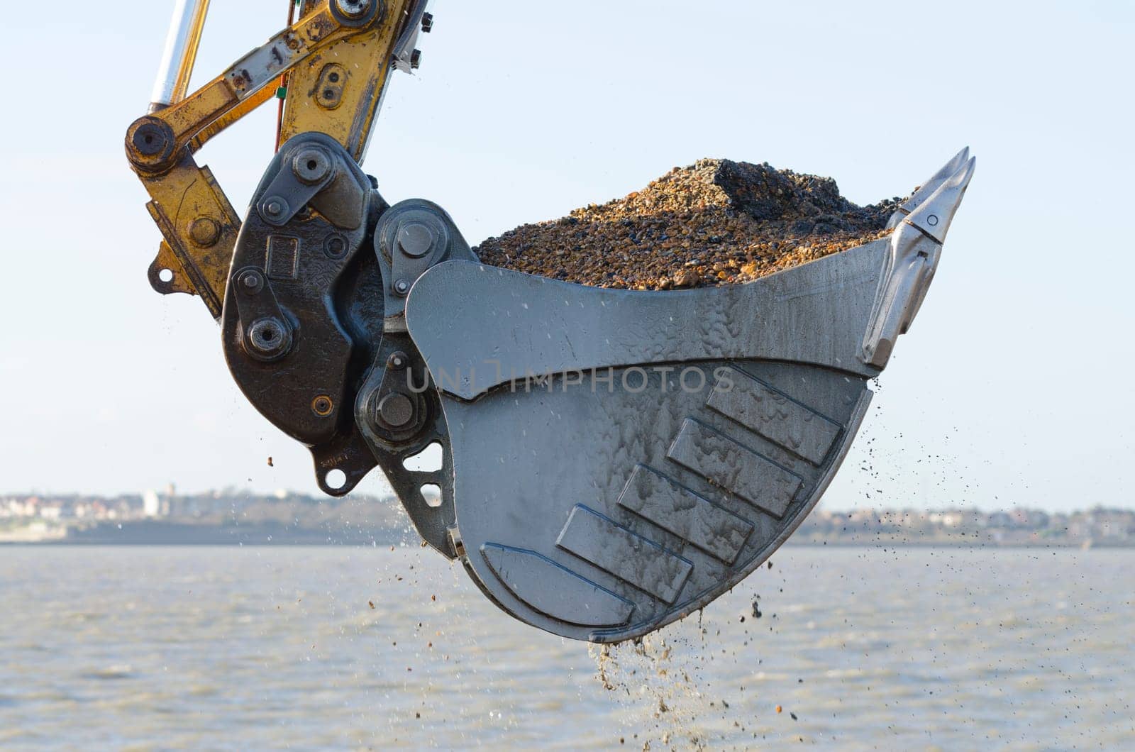 Excavator bucket dredging sand and gravel from the seafront