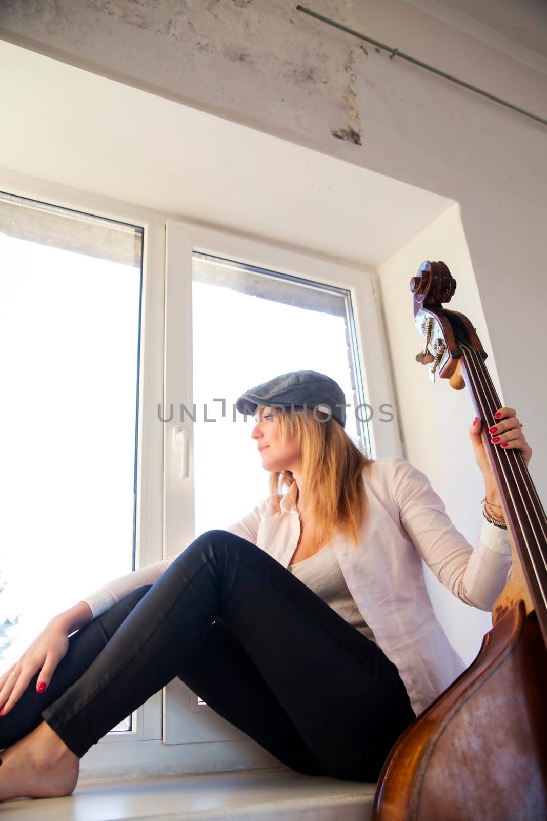 Charming woman barefoot on white windowsill and contrabas