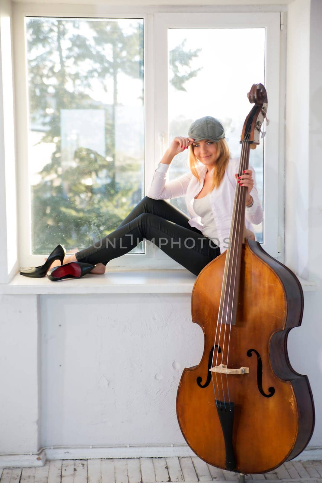 Charming woman with hat on windowsill and contrabass