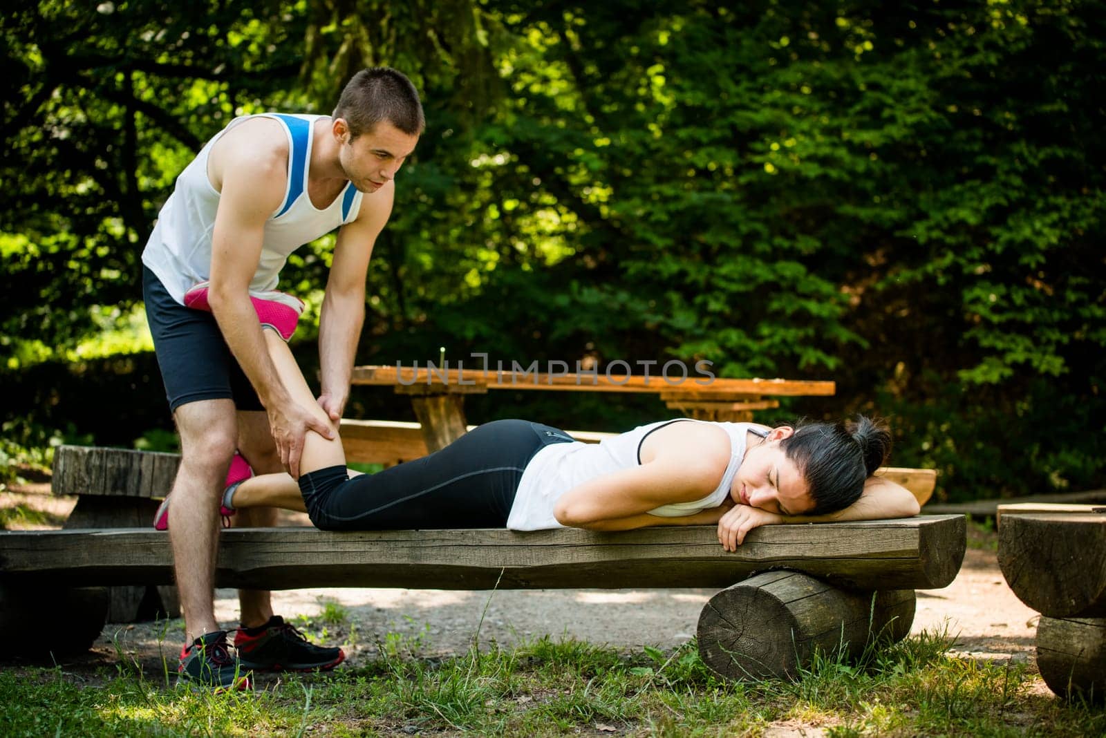 Man gives massage of calf to his girlfriend after sport training - woman lies on bench