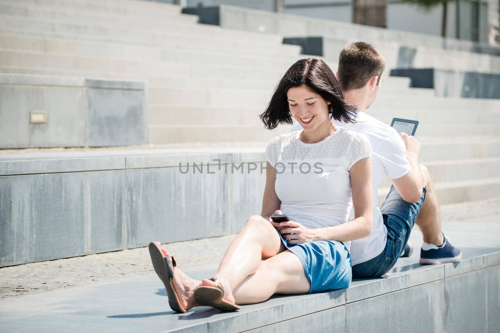 Young couple in street - woman with smartphone, man with tablet