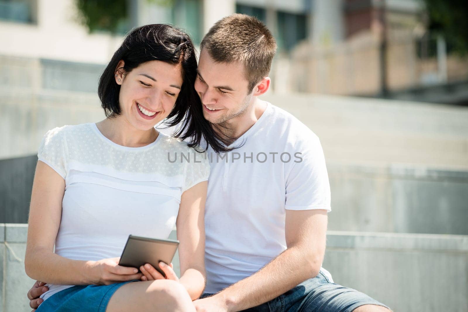 Young happy couple smiling over something in tablet - outdoor