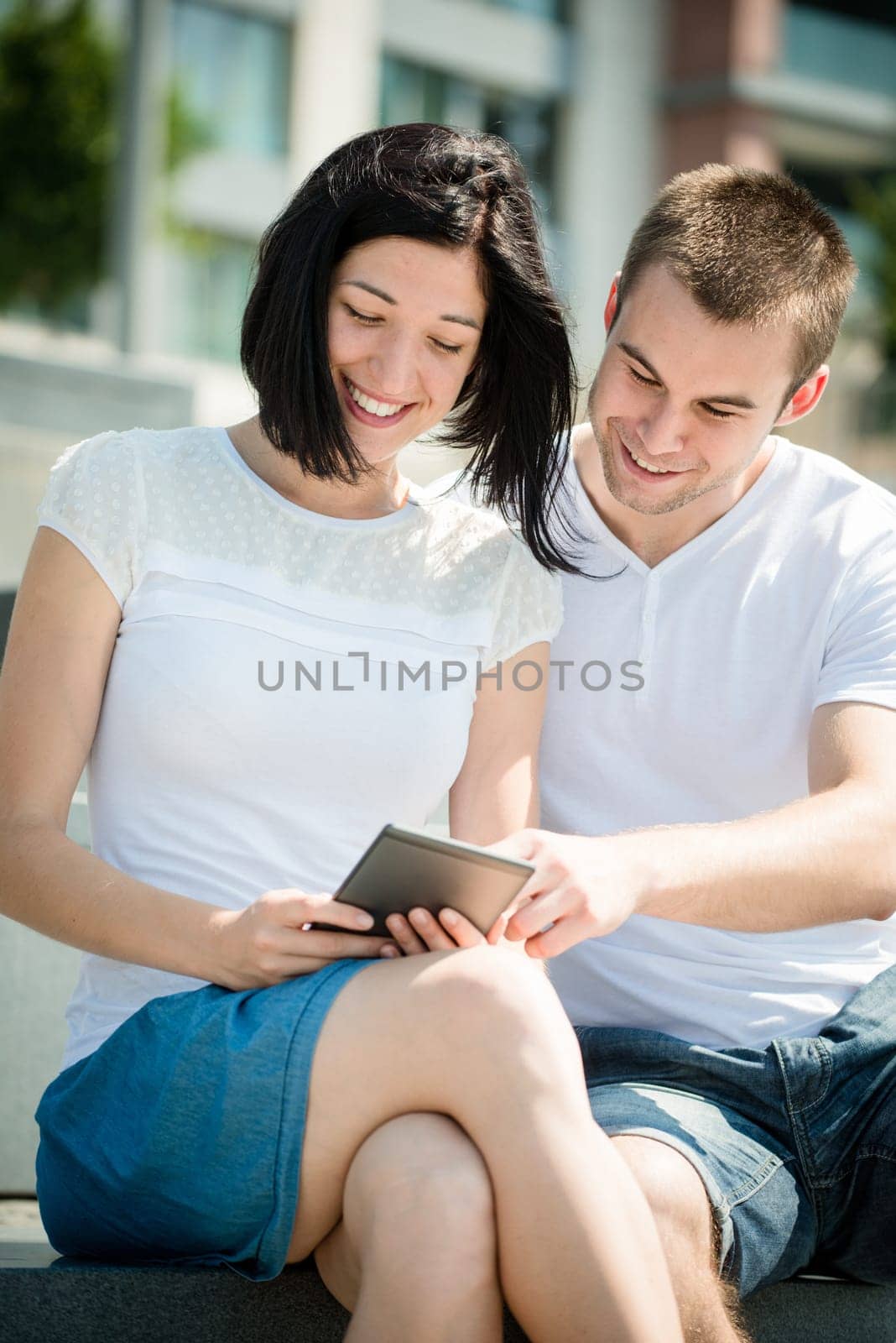 Young happy couple smiling over something in tablet - outdoor