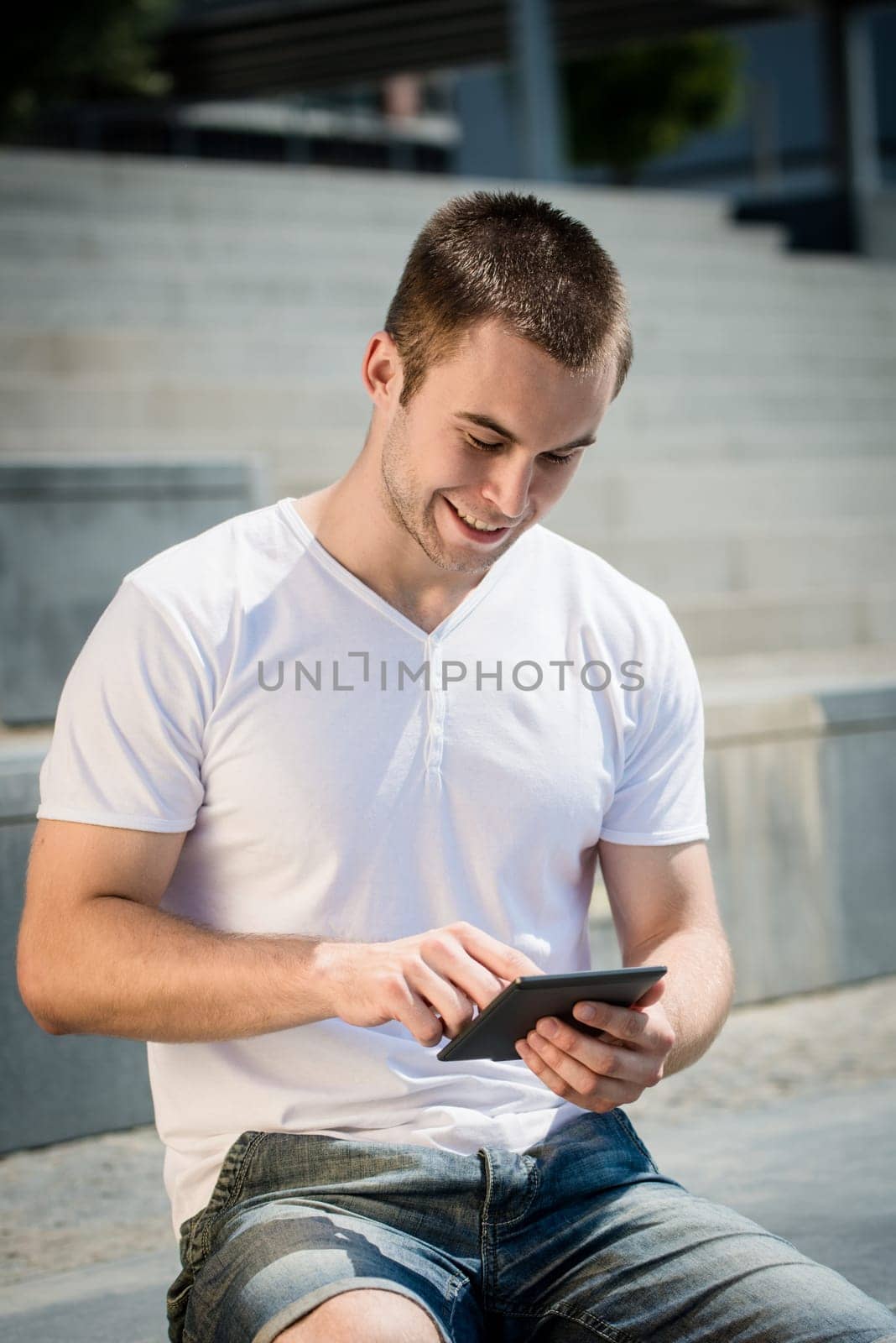 Young man reading book on electronic book-reader in urban environment