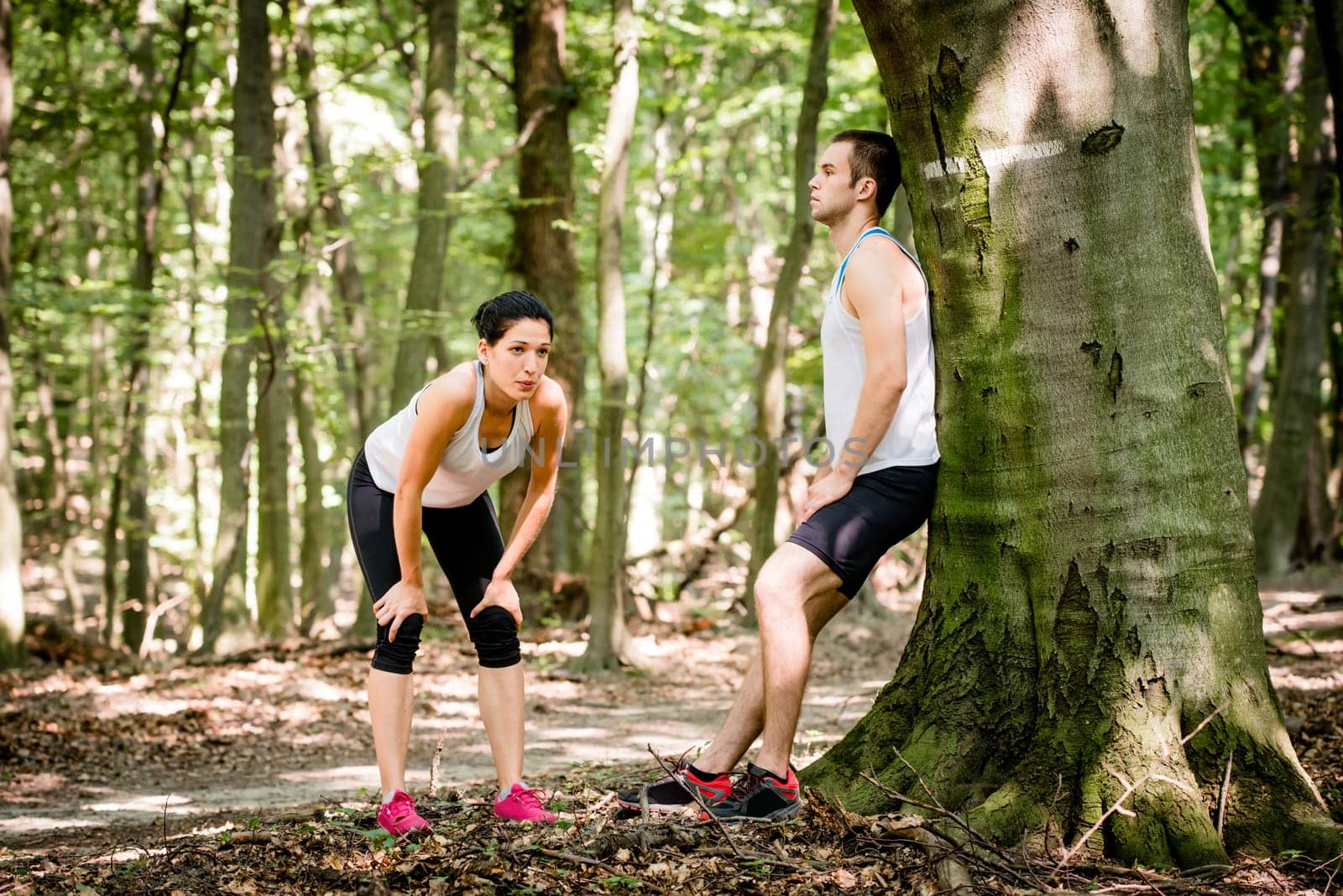 Young couple resting after jogging in nature, man leans against tree