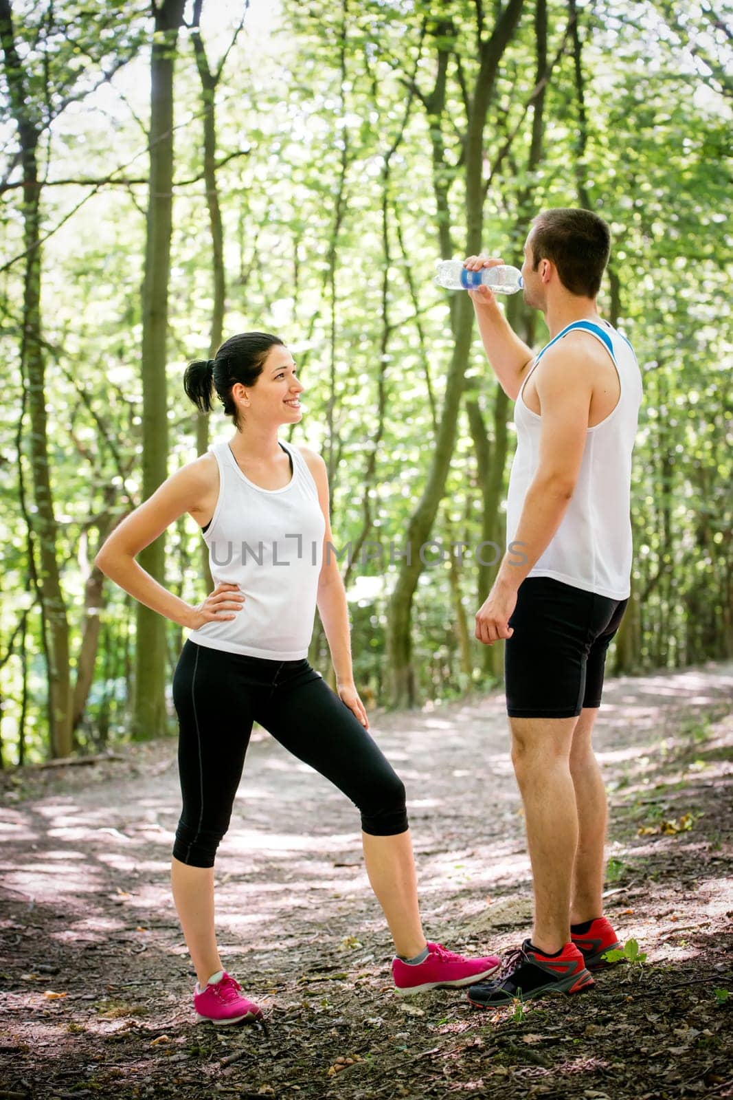 Young couple relaxing after jogging in nature, man drinking water