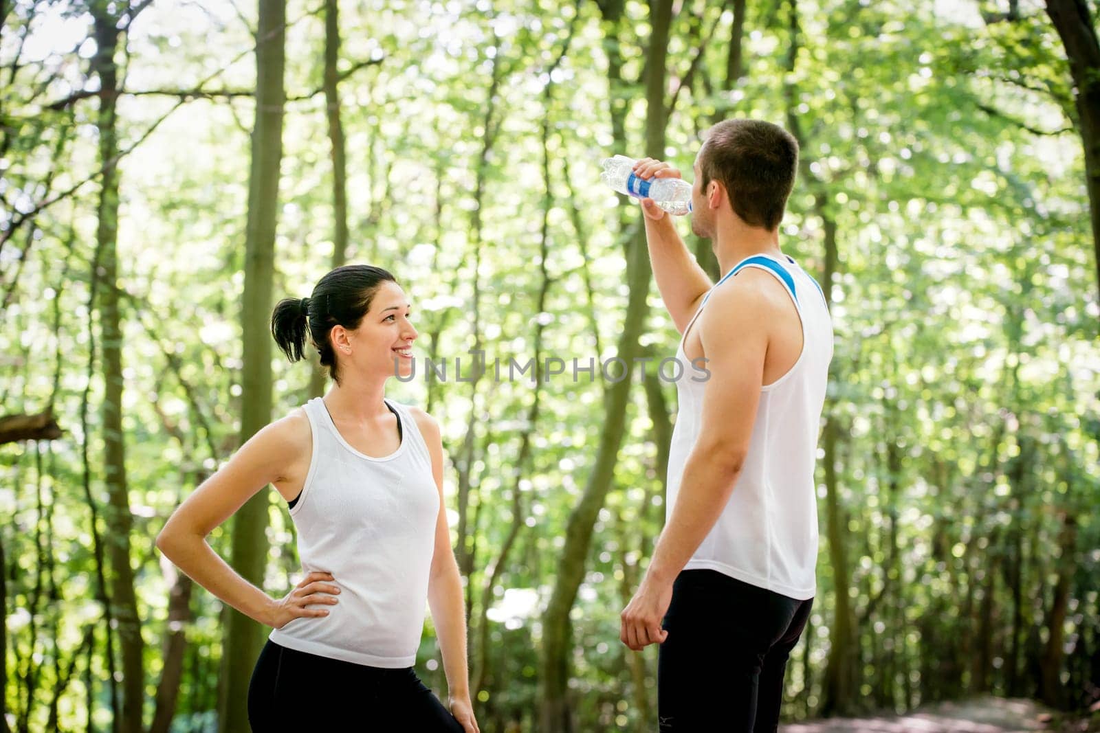 Young couple relaxing after jogging in nature, man drinking water