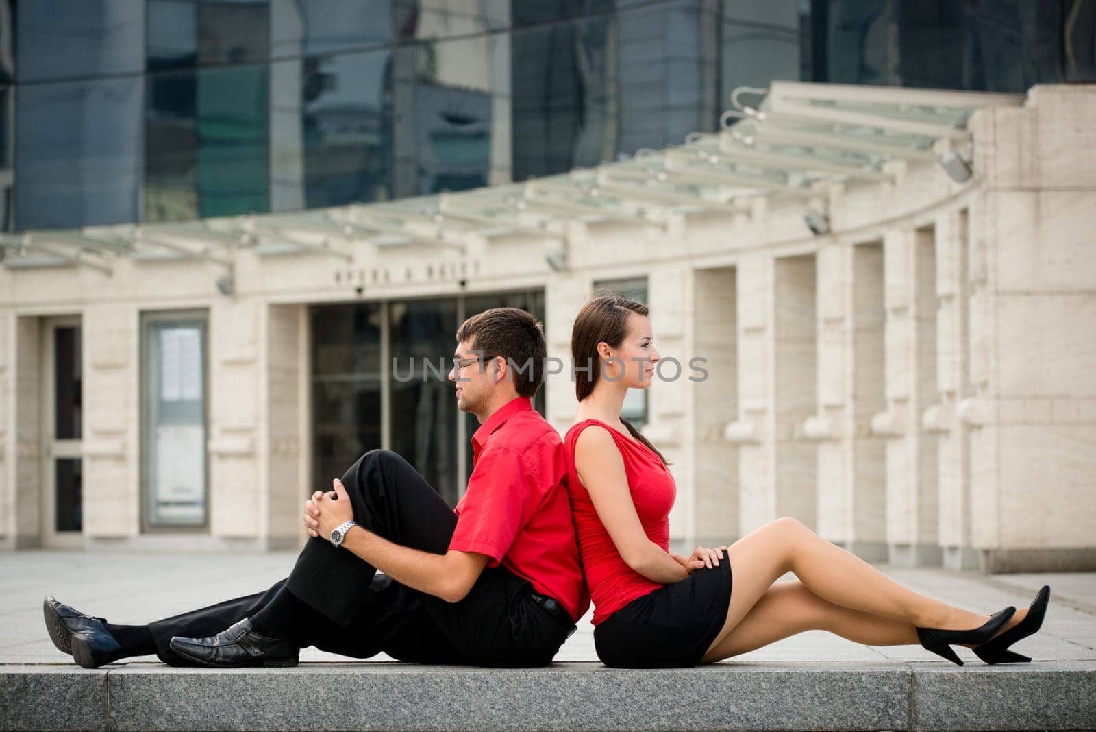 Young business couple relaxing leant with backs on street