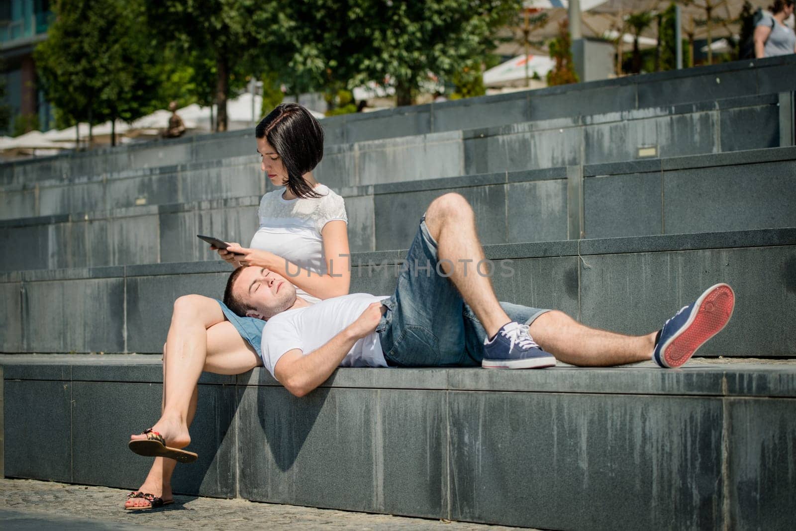 Young couple relaxing - woman with tablet, man lying on her tights
