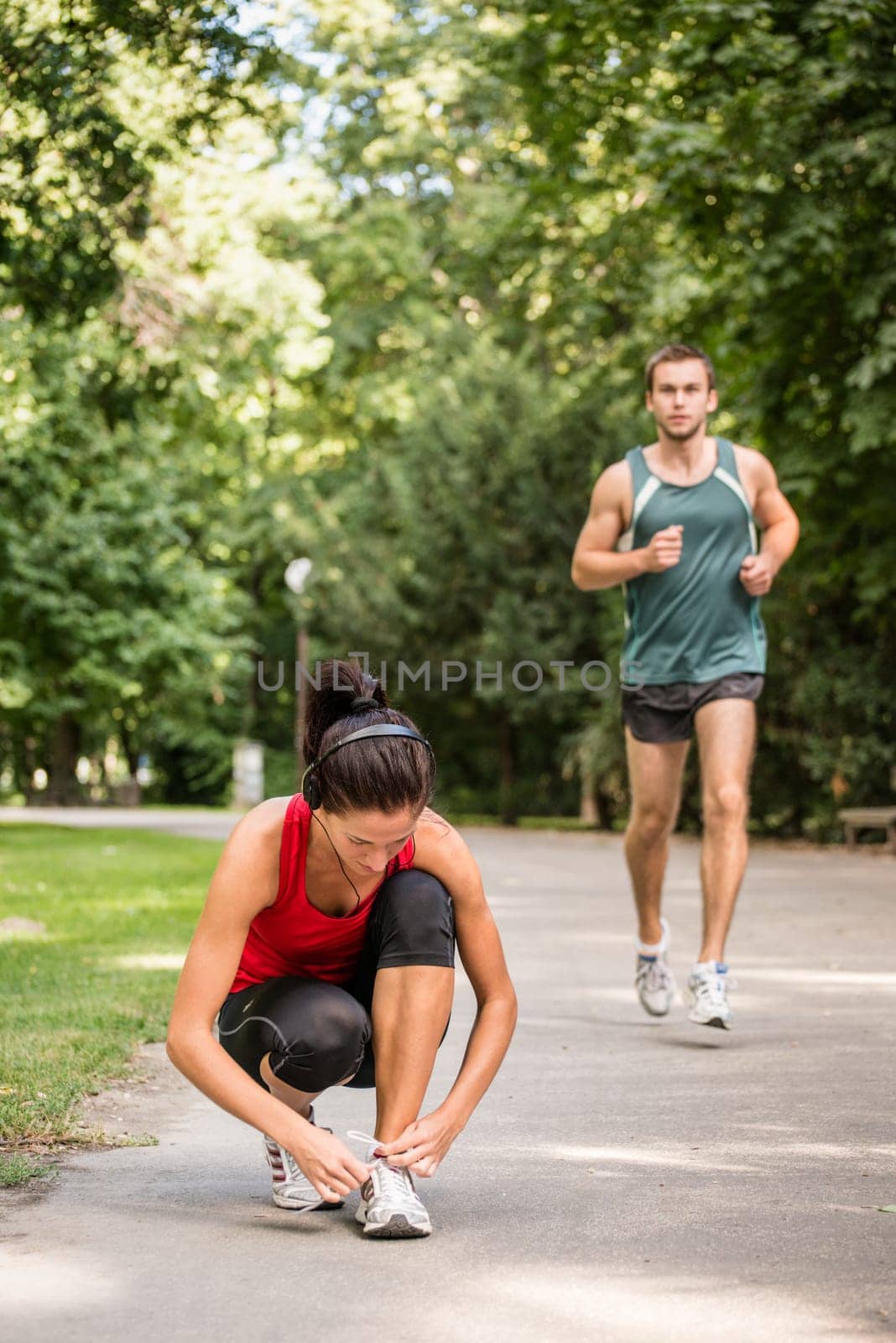 Young sport woman tying shoelace, man in behind is jogging