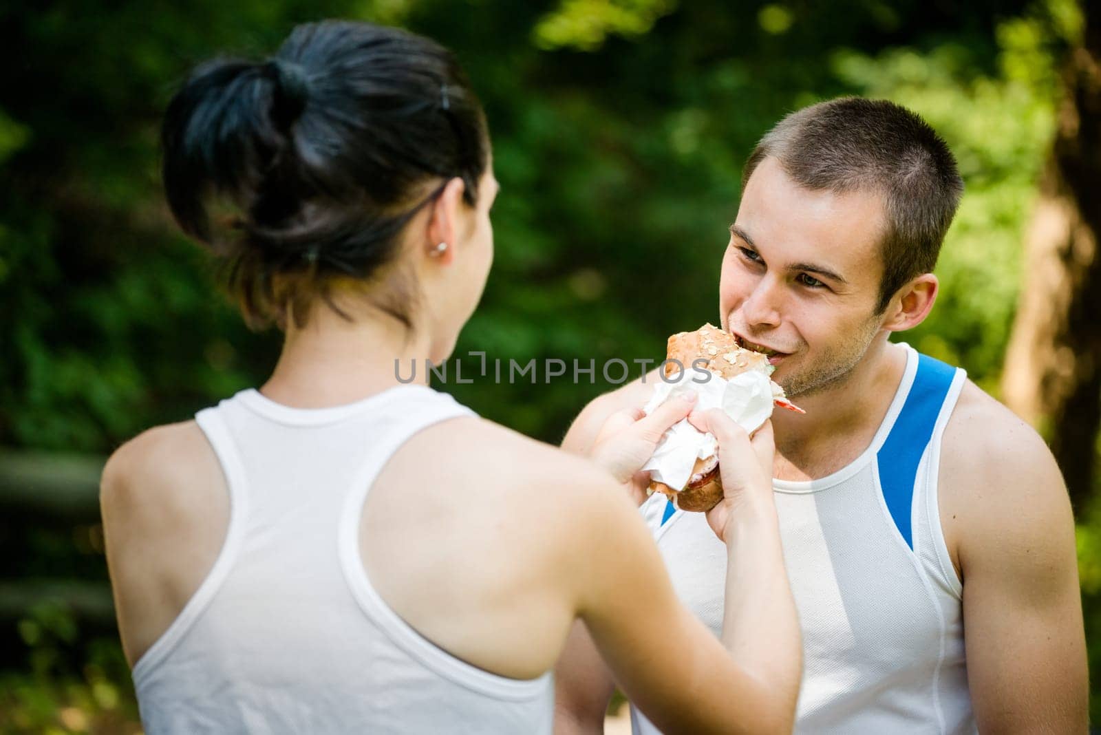 Young couple eating after sport training outdoor in nature - woman feeds man