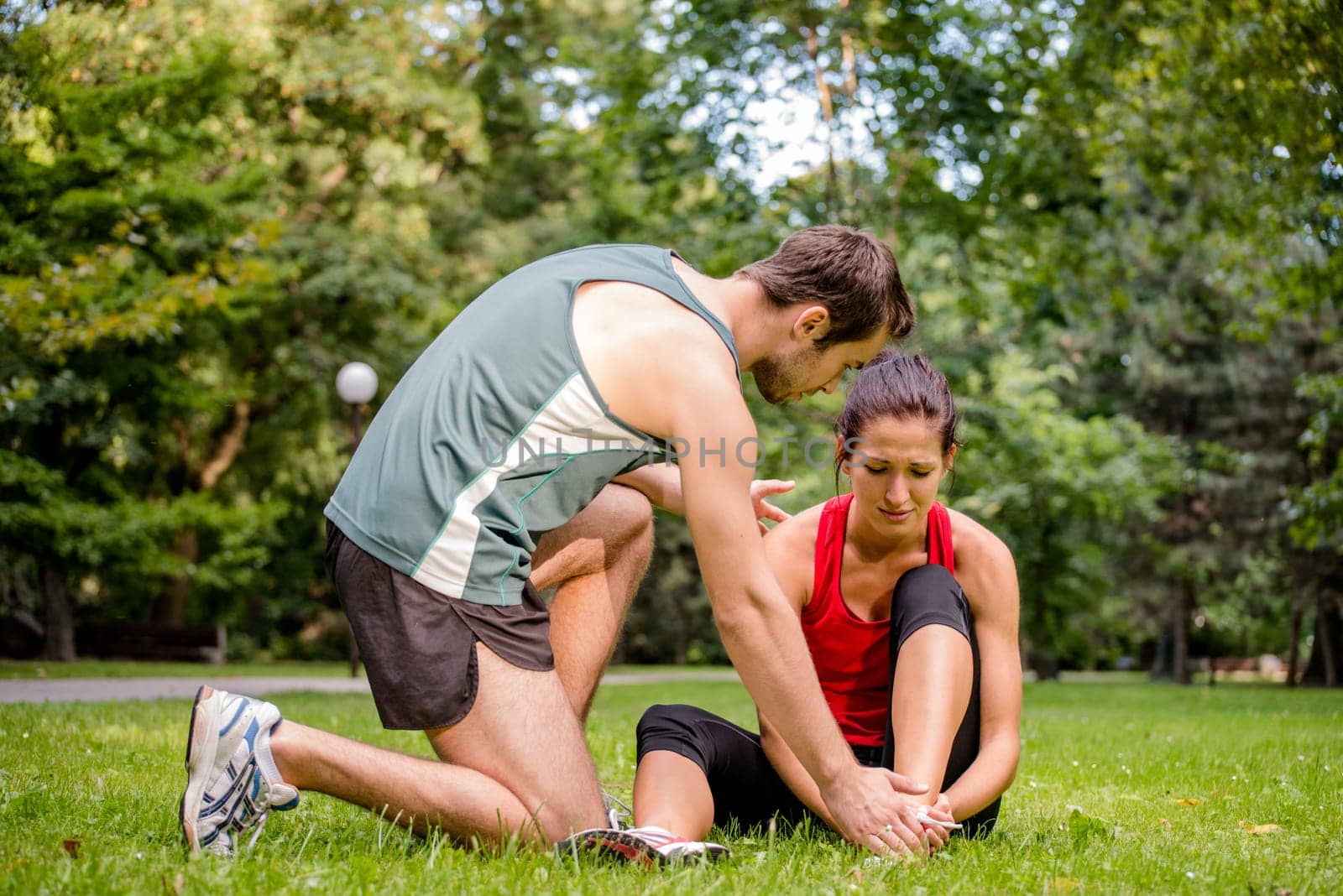 Sport injury - young fitness woman holding her ankle  with pain, man is helping