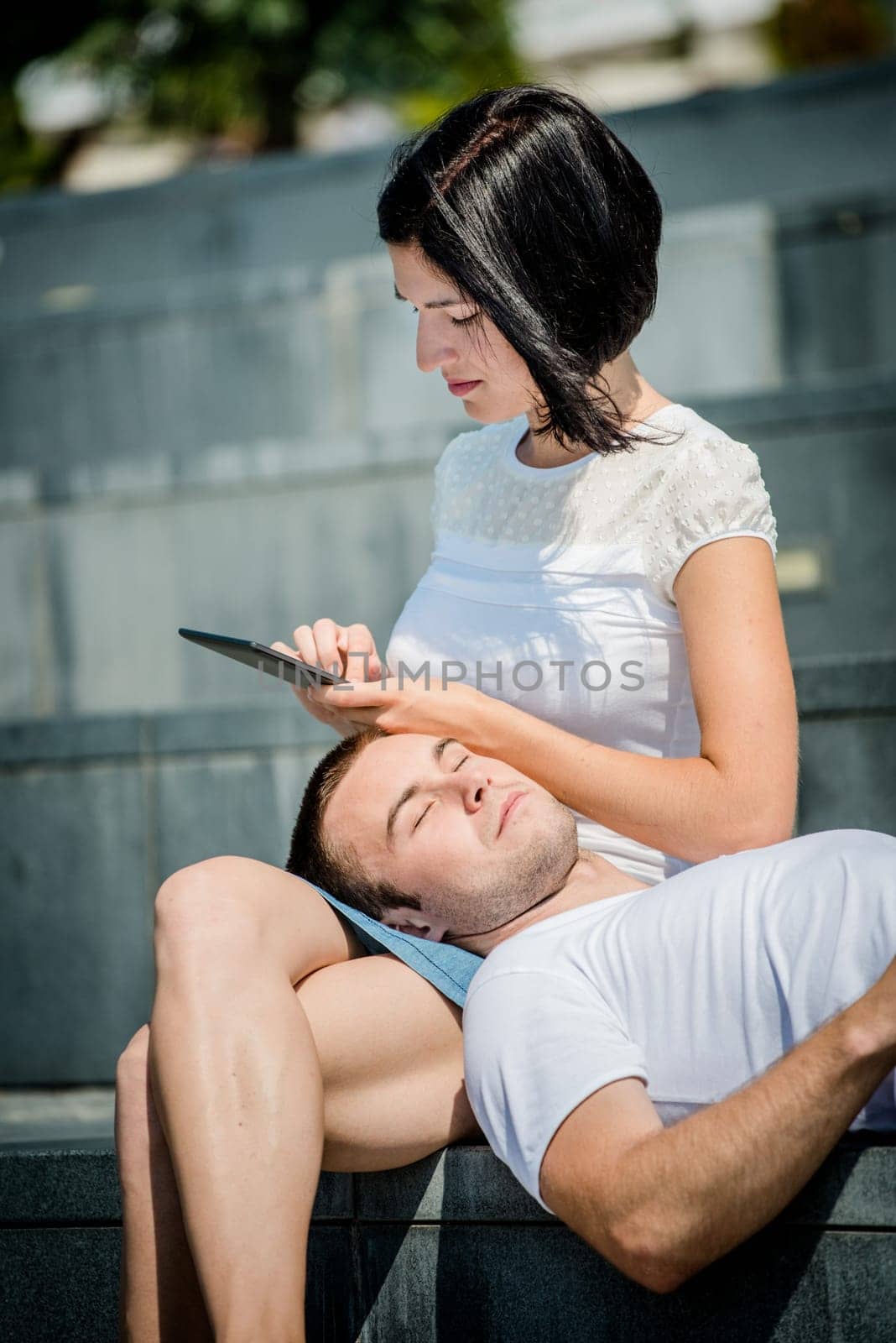 Young couple relaxing - woman with tablet, man lying on her tights