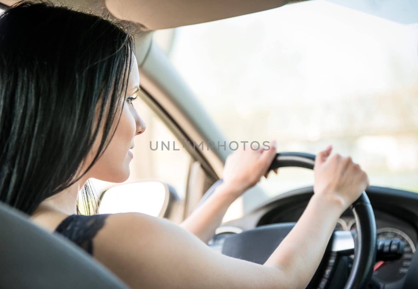 Young beautiful black-haired woman driving car - rear view
