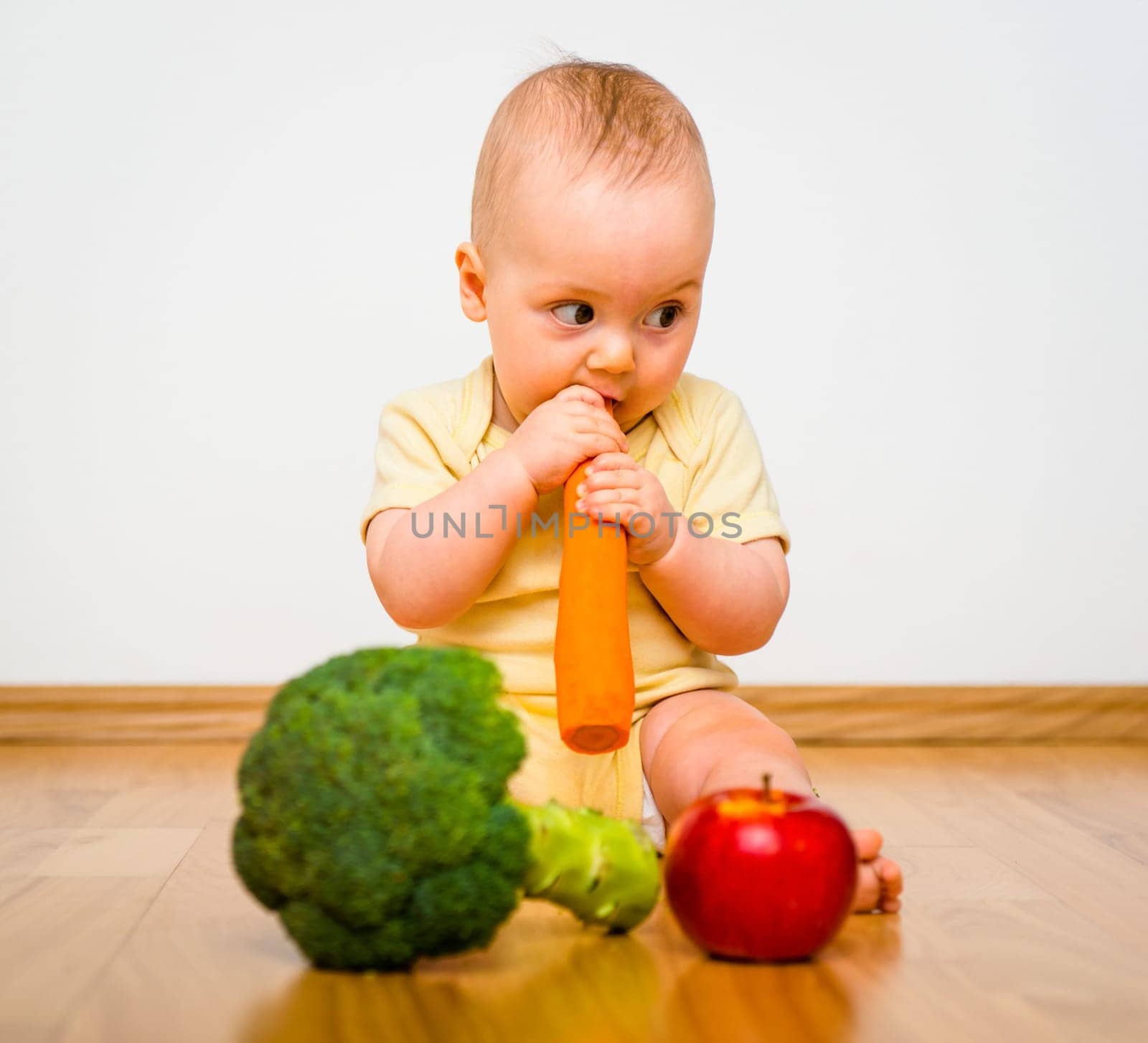 Healthy living. Baby eating fruit and vegetables - sitting on floor