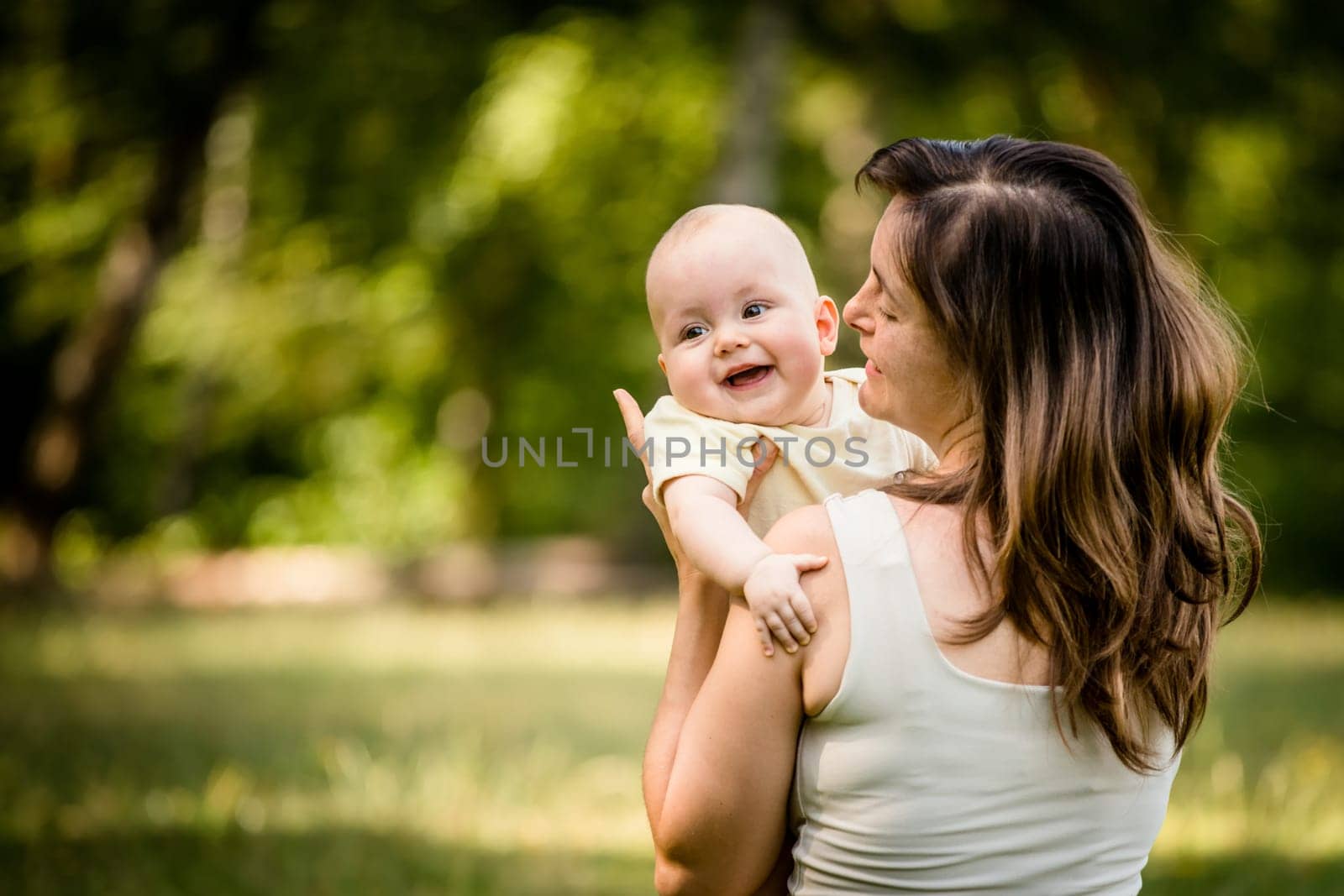 Happy mother holding her baby on hands outdoor in nature