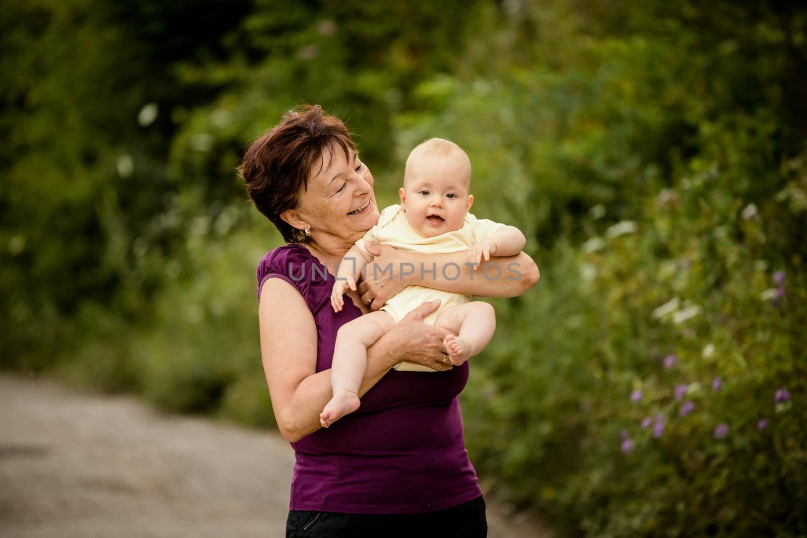 Grandmother with grandchild - senior woman holding her granddaughter outdoor in nature
