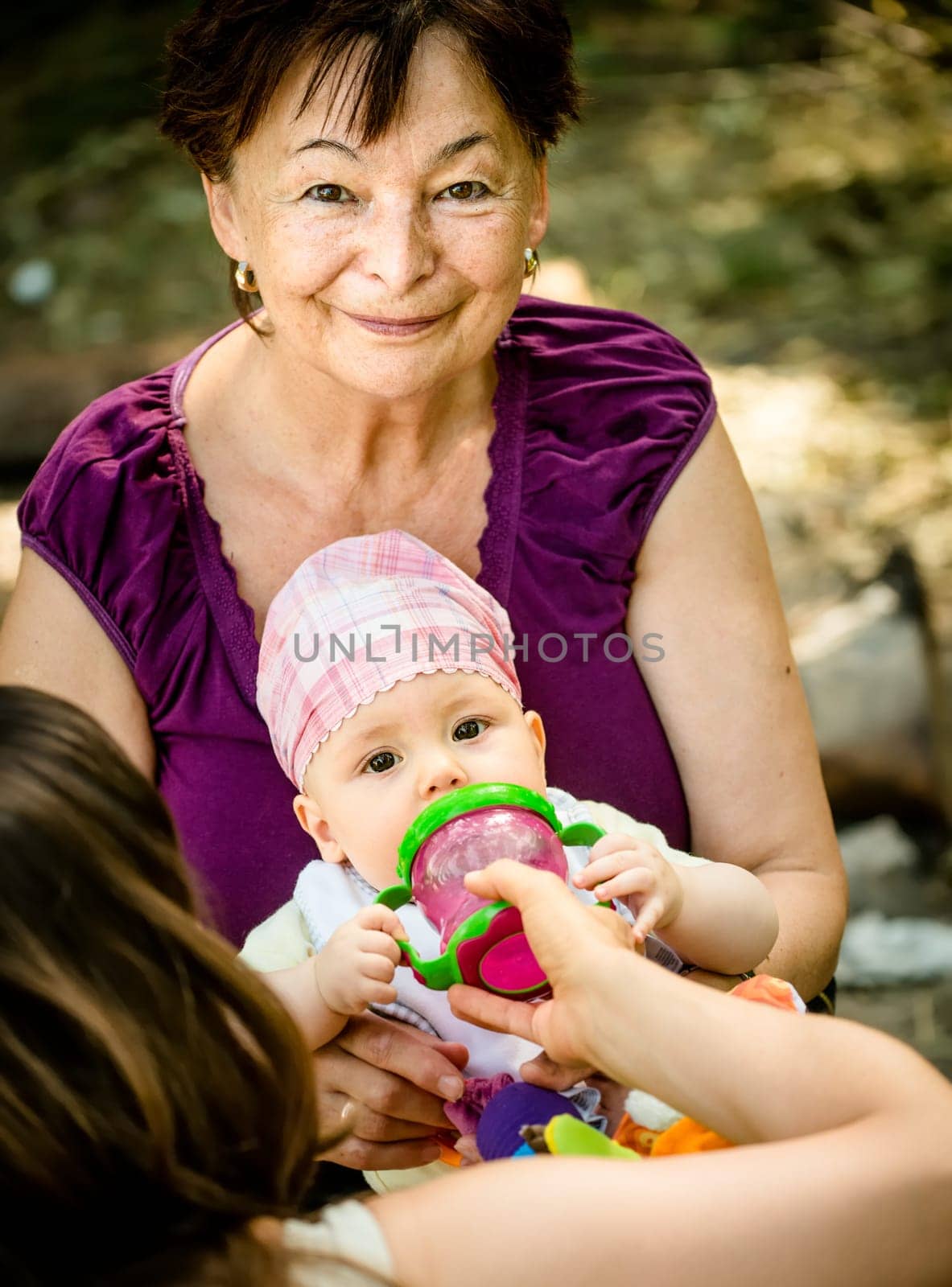 Mother gives a drink from bottle to her baby, grandmother is helping