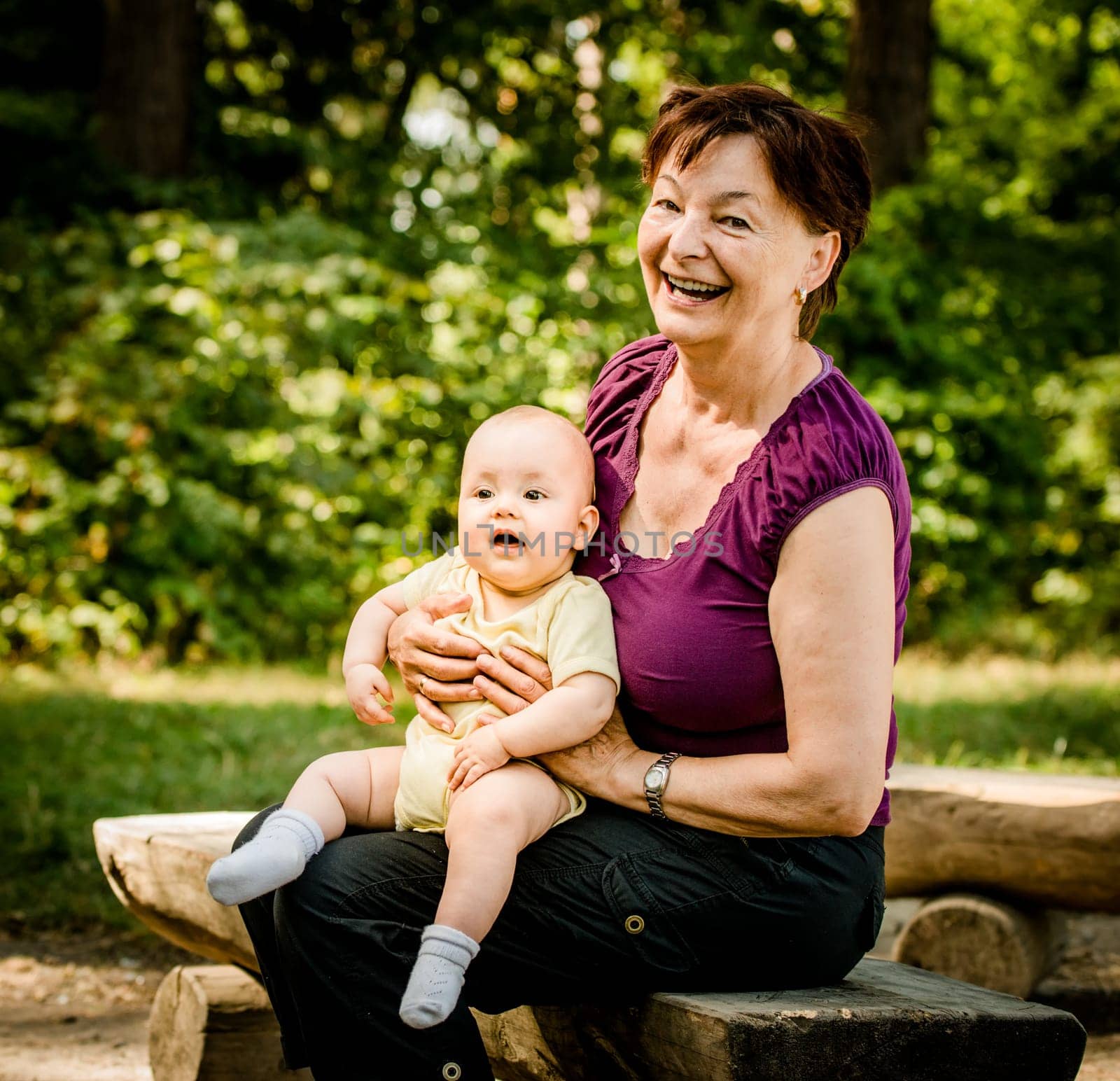 Grandmother with grandchild - senior woman sitting with her granddaughter on bench outdoor in nature