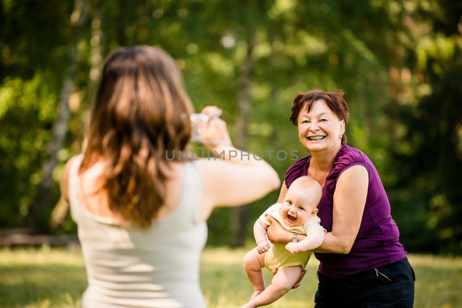 Mother taking photo of grandmother holding her granddaughter - outdoor in nature