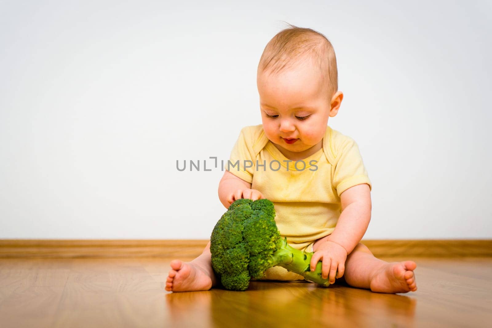 Cute baby exploring broccoli - sitting on floor indoors