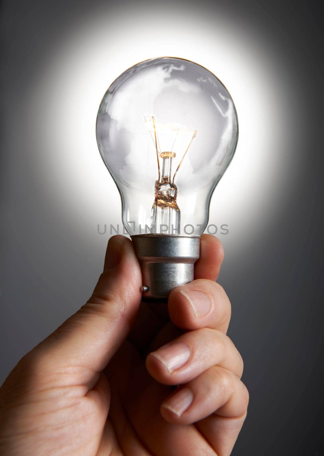 Mans hand holding a light bulb against grey background