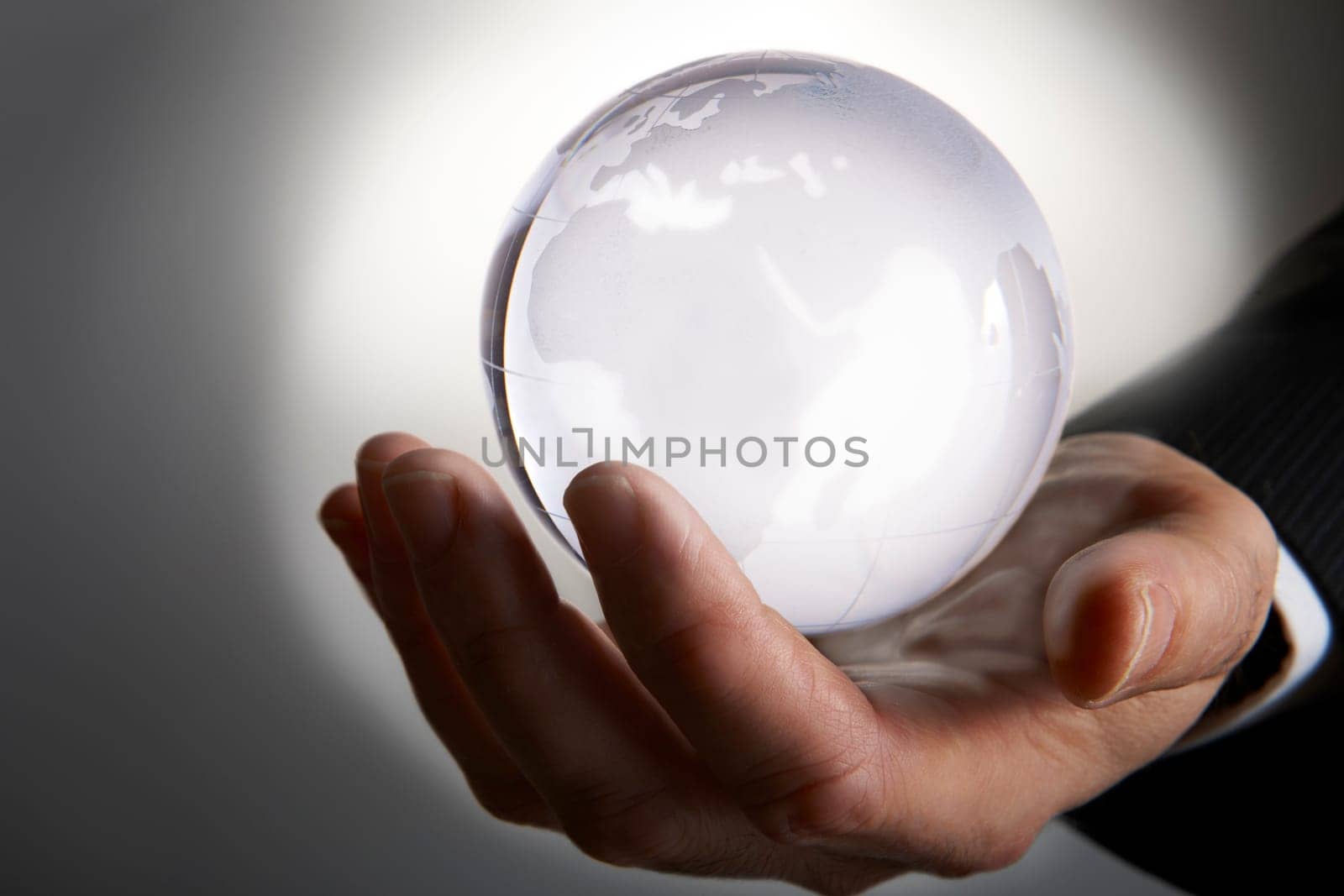 Businessmans hand holding glowing glass globe in palm against grey background