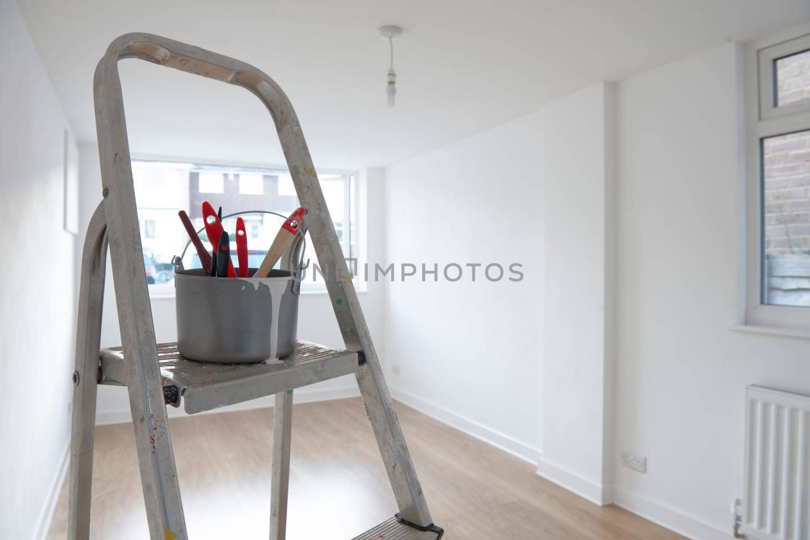 ladder with paint pot and brushes standing in empty room