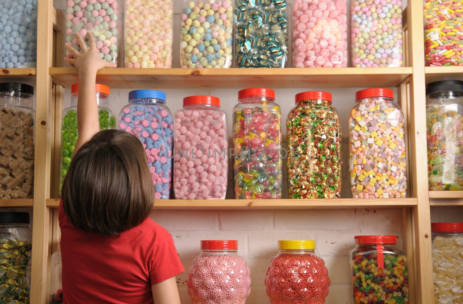 young girl reaching for sweet jar on top shelf