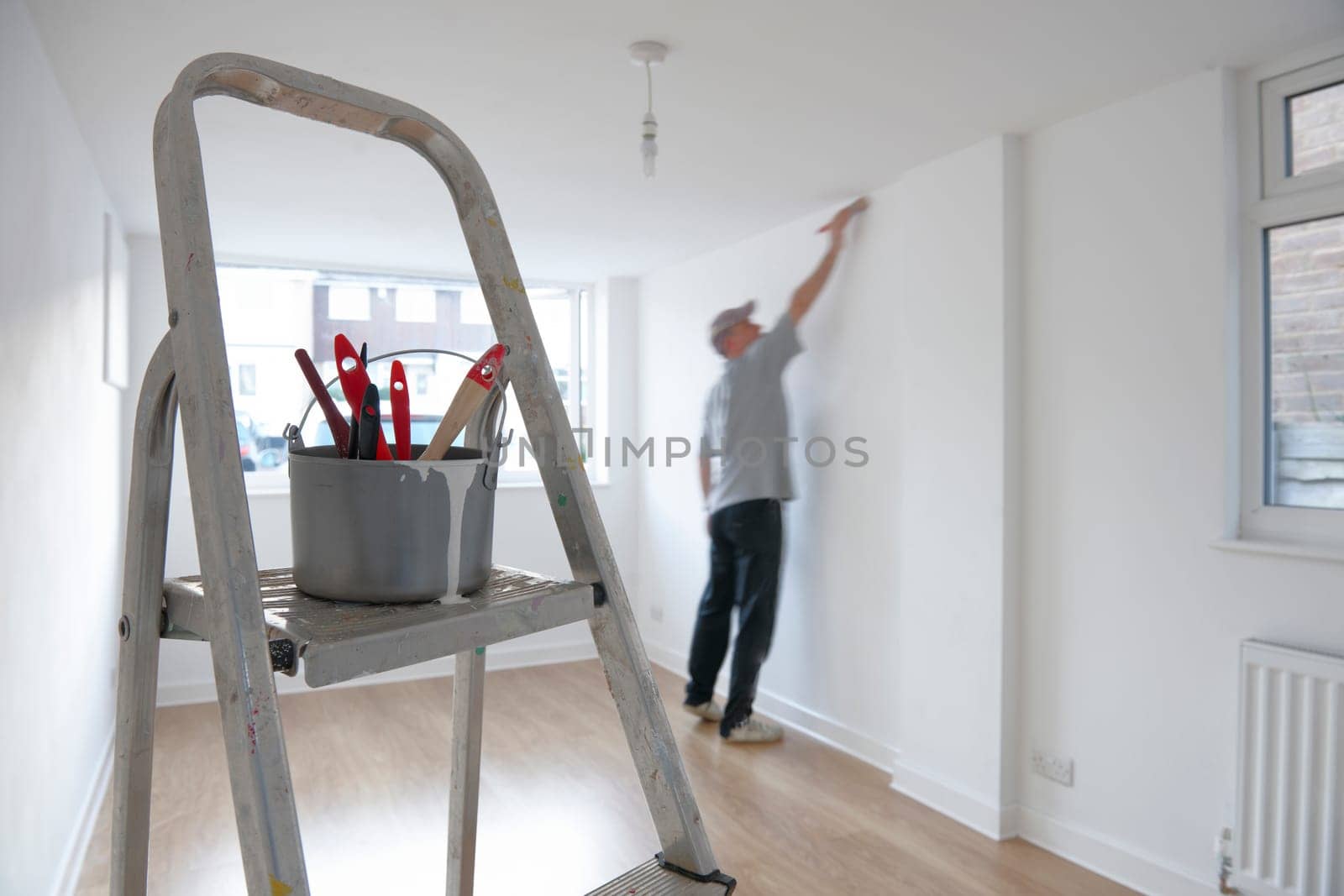 man decorating a room with ladder and paint pot in foreground