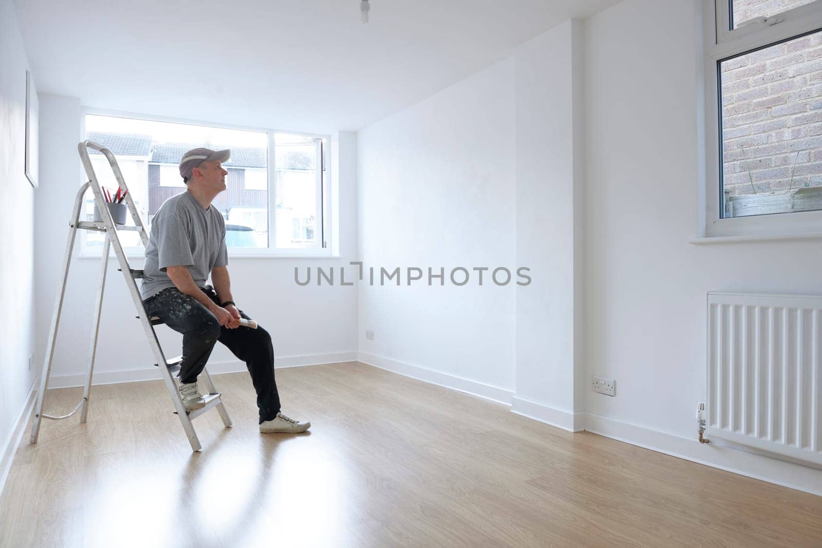 man sitting on ladder looking at newly decorated white painted room