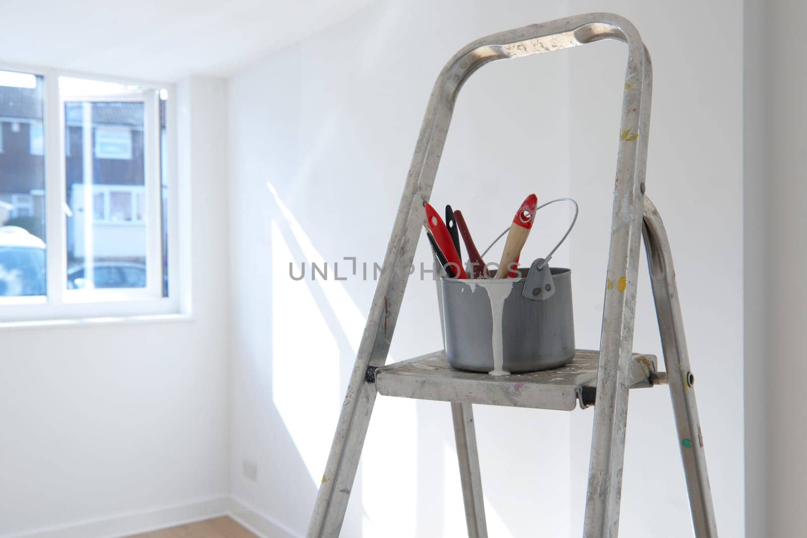 ladder with paint pot and brushes standing in empty room