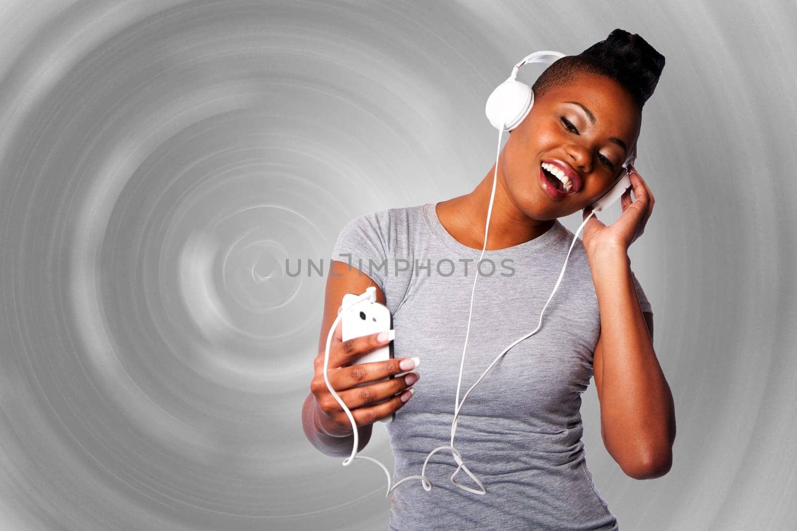 Beautiful young woman with headphones and mobile device listening grooving singing to music, gray circular background.