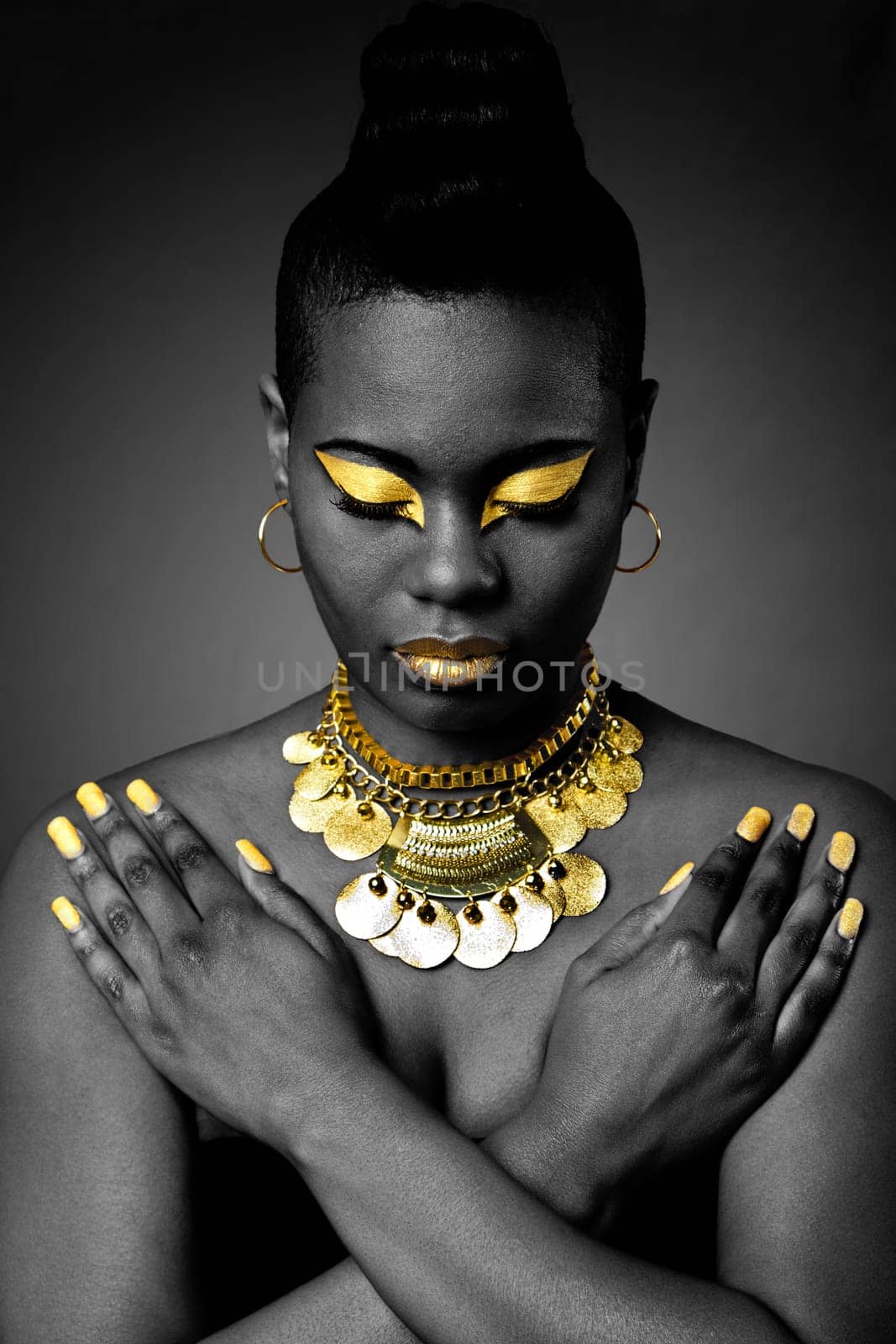 Beautiful African tribal fashion with gold eyeshadow and necklace on dark with arms crossed and looking down.
