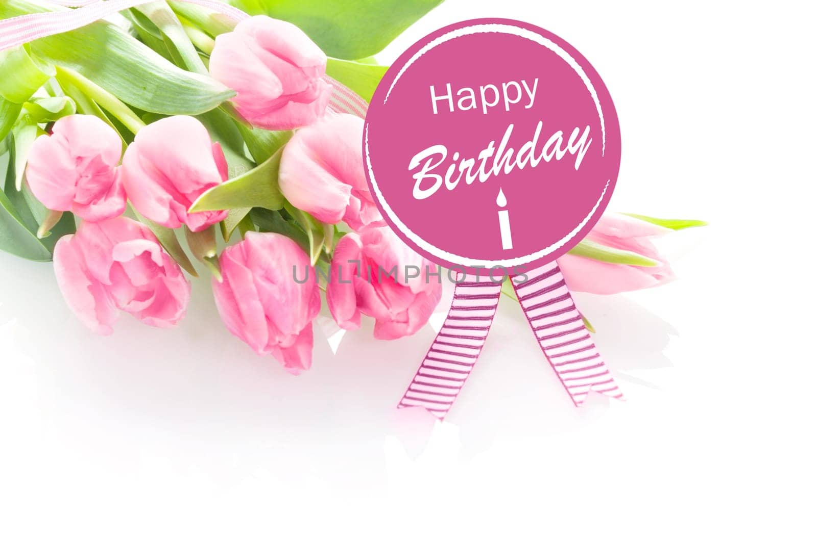 Bunch of beautiful fresh pink tulips with a Happy Birthday greeting message on a round purple rosette with festive ribbons over a white background
