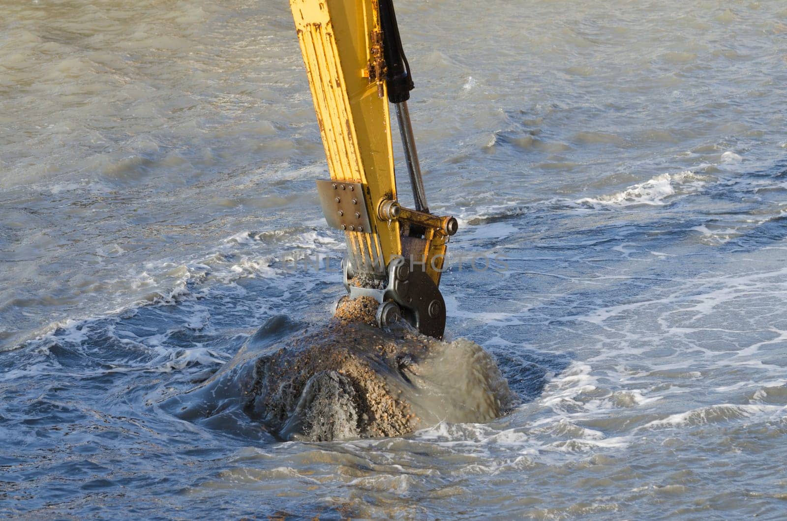 Excavator bucket dredging sand and gravel from the seafront