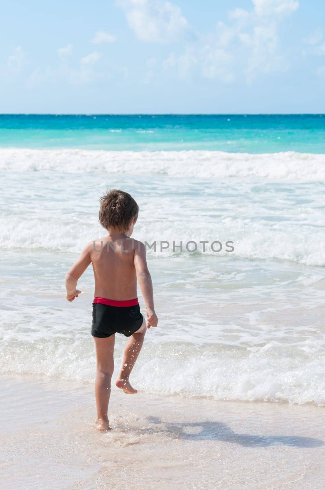 Blond boy runs into the turquoise sea in the Caribbean.