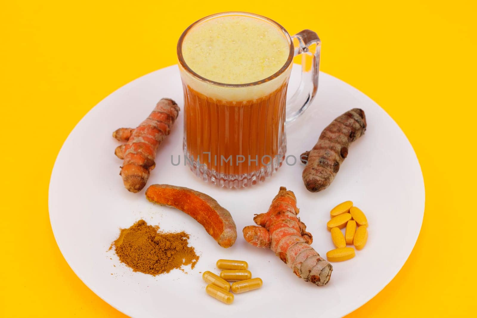 Turmeric juice beverage cup, three fresh and raw conventional rhizome roots, one turmeric root partially peeled, standardized extract capsules and tablets, along with some dry ground turmeric powder.
