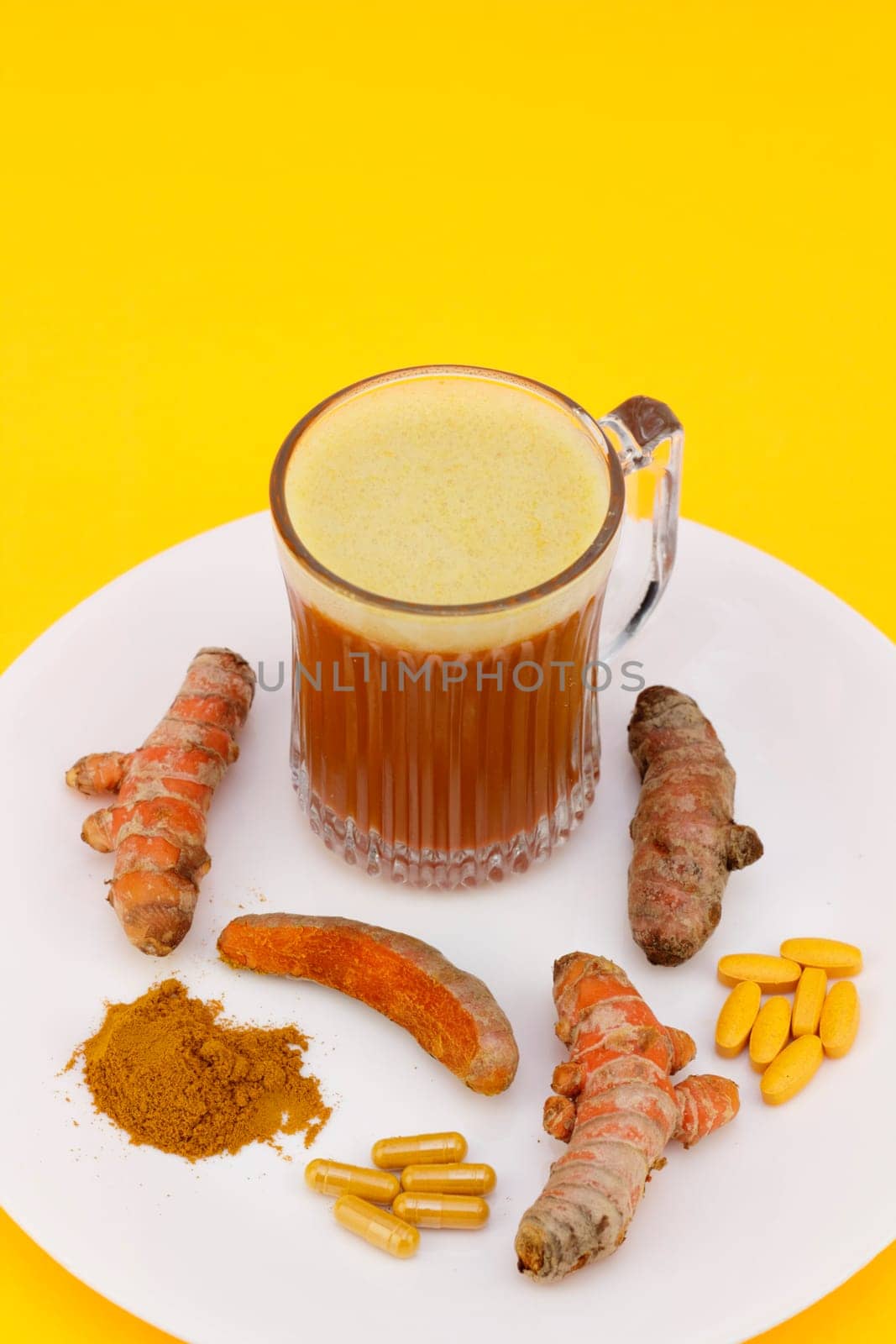 Standardized extract in pills and capsules, ground powder, slightly peeled and whole rhizome roots with a blended beverage of turmeric on a white plate with an orange background.