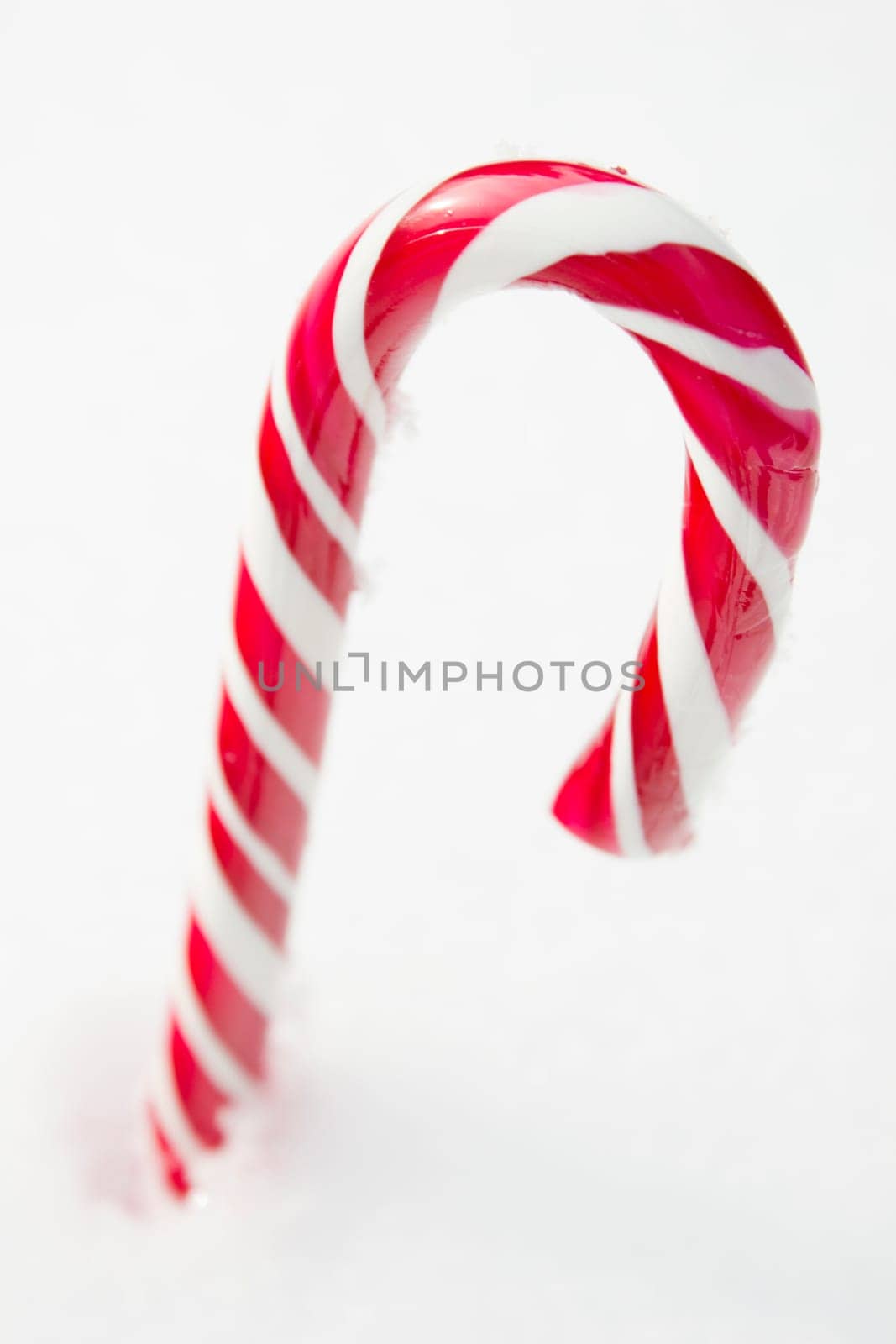 Sweet red and white candy cane lying in the snow.